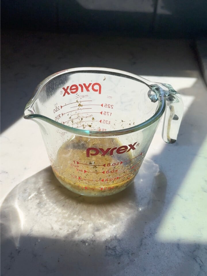 A garlic and herb marinade is mixed in a glass measuring cup before being poured over the chicken and potatoes.