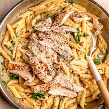 Overhead view of creamy garlic Parmesan chicken pasta with penne, spinach, sliced chicken, red pepper flakes and grated Parmesan.
