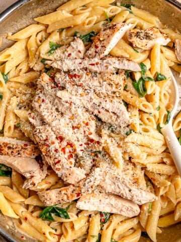 Overhead view of creamy garlic Parmesan chicken pasta with penne, spinach, sliced chicken, red pepper flakes and grated Parmesan.