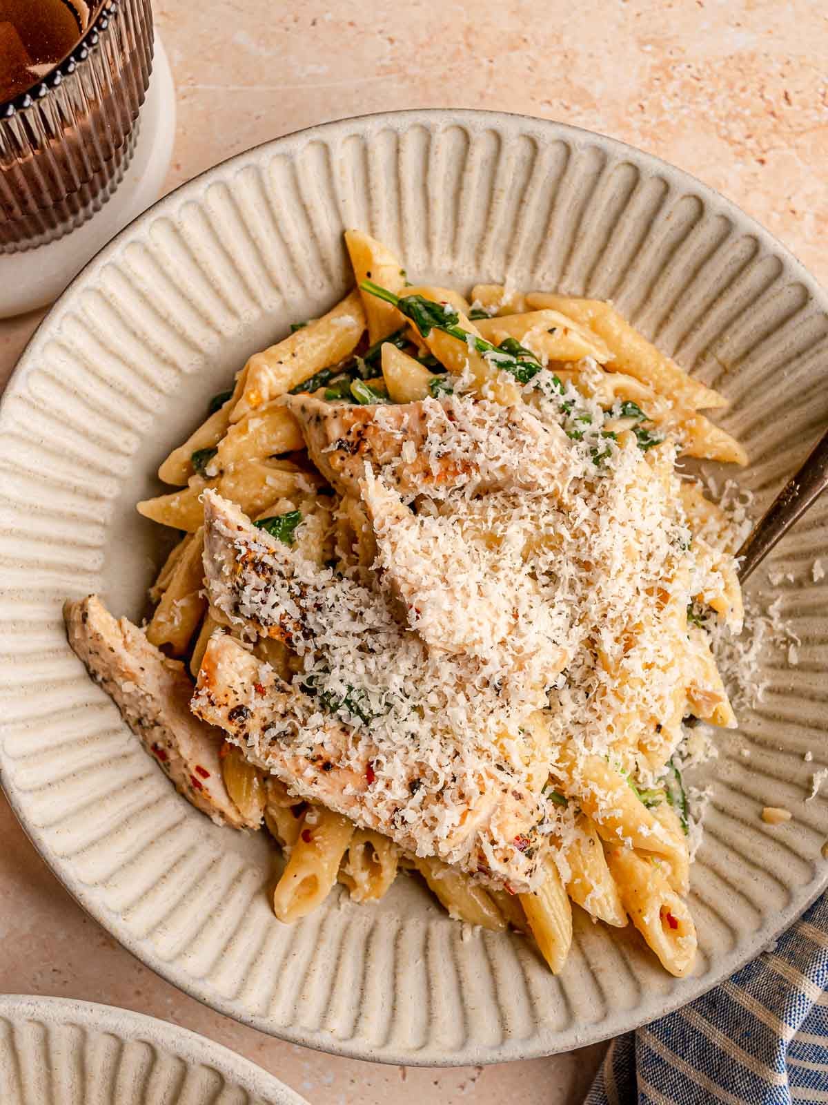 Plate of creamy garlic Parmesan chicken pasta with penne and spinach, generously topped with freshly grated Parmesan.