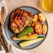 Herb-marinated grilled chicken thigh plated with roasted potatoes and zucchini.