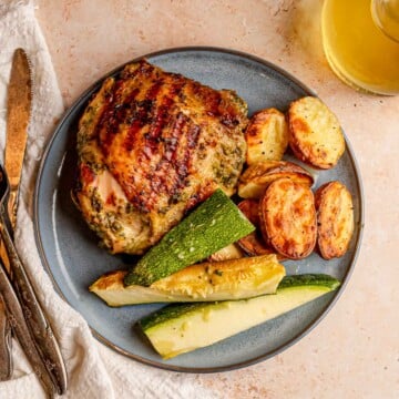 Herb-marinated grilled chicken thigh plated with roasted potatoes and zucchini.