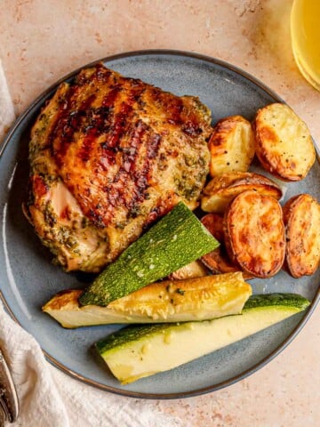 Herb-marinated grilled chicken thigh plated with roasted potatoes and zucchini.