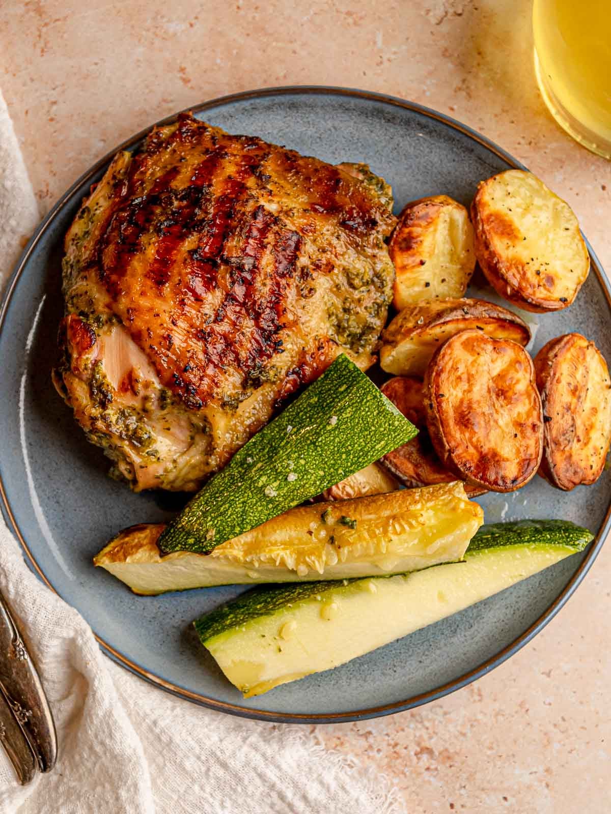 Herb-marinated grilled chicken thigh served with roasted potatoes and zucchini.