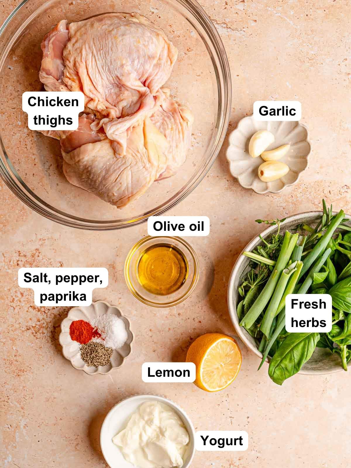 Ingredients for herb-marinated chicken thighs: chicken, garlic, olive oil, lemon, yogurt, fresh herbs, salt, pepper and paprika.