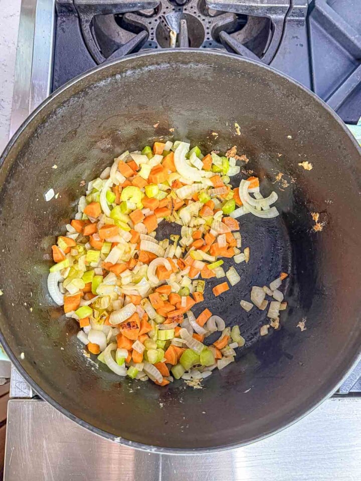 Chopped onion, carrots, and celery sauté in a large pot to form the vegetable base for Italian wedding soup.