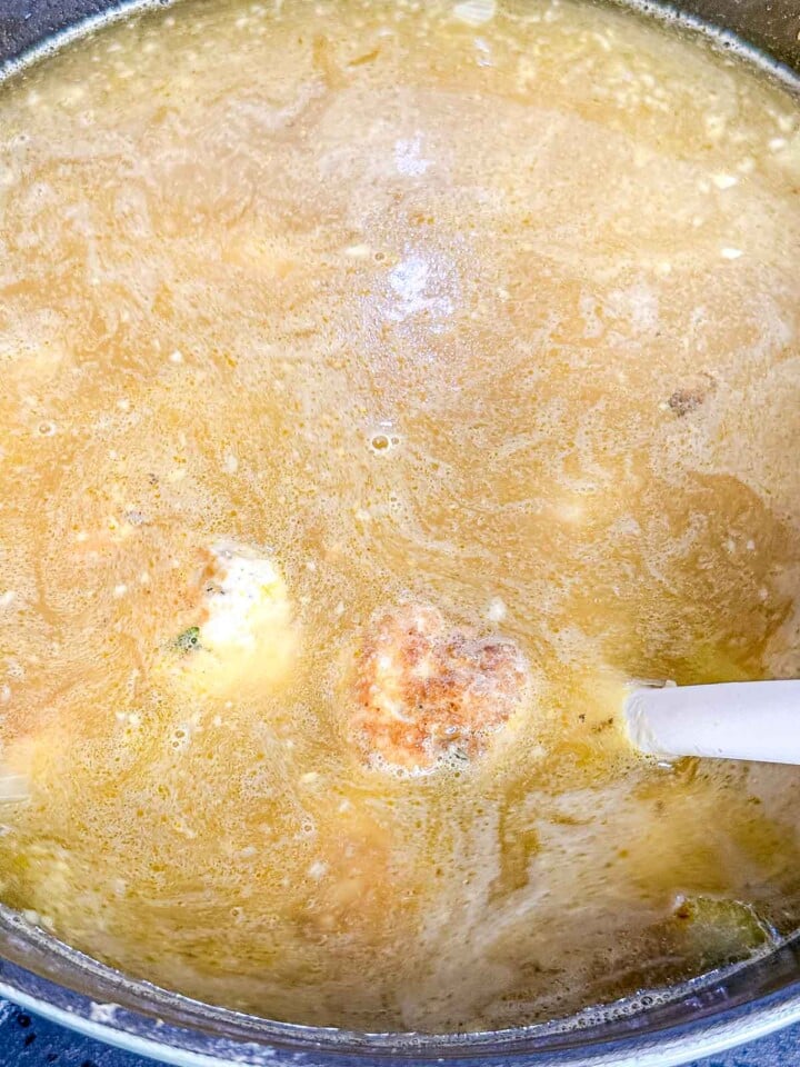 Chicken broth simmers in a large pot with browned chicken meatballs as the soup cooks.