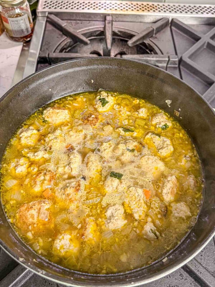 Chicken meatballs simmer with vegetables in a golden chicken broth in a large pot.