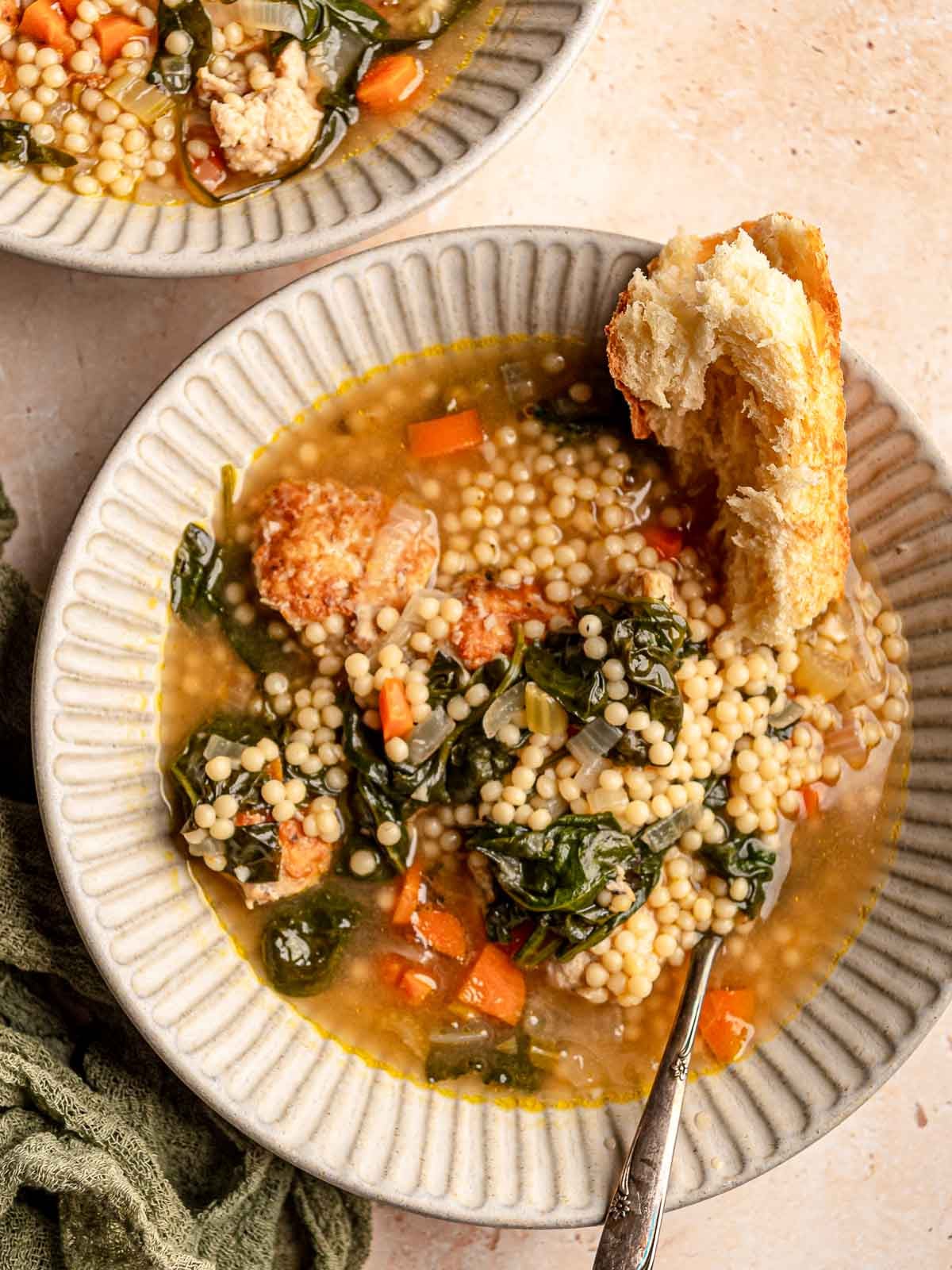 Italian wedding soup with chicken meatballs, acini di pepe, spinach, carrots, and celery is served with crusty bread.