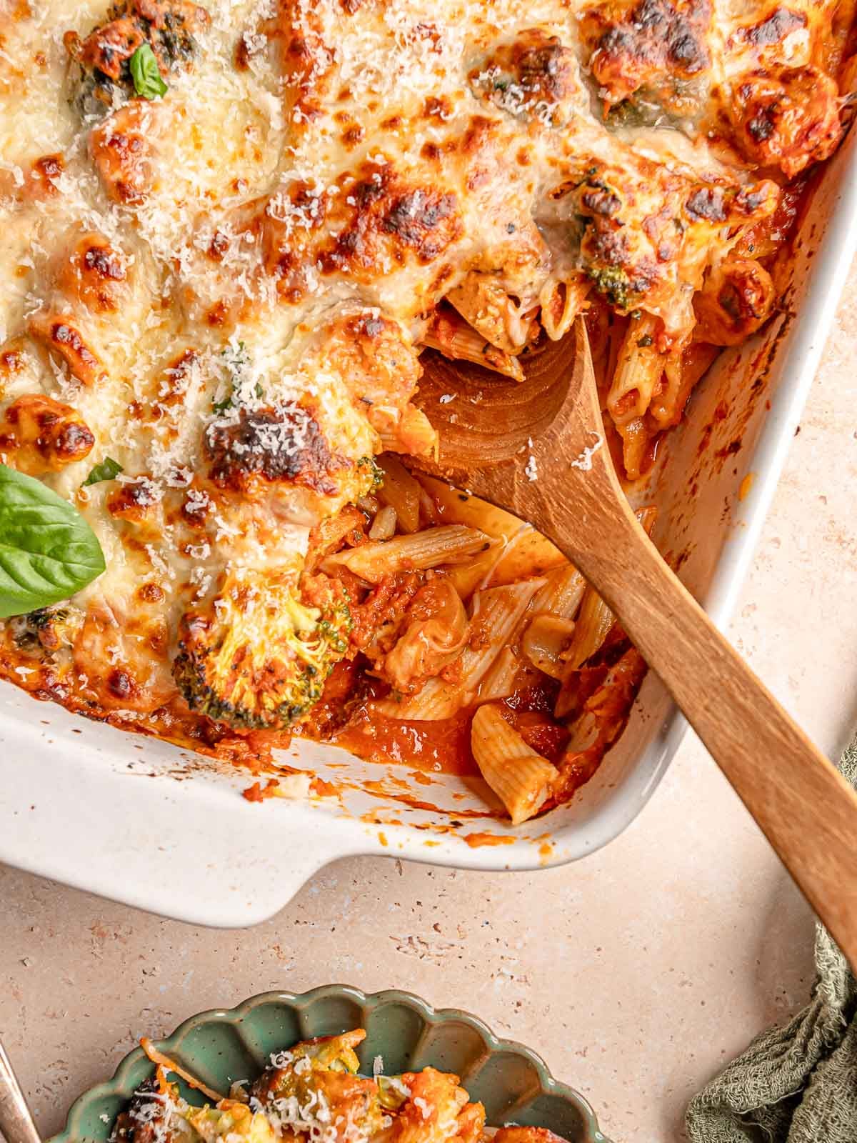 No-boil pasta bake being served from a casserole dish onto a plate, revealing saucy penne, sausage and broccoli.