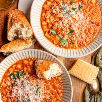 Bowls of thick pasta e fagioli are topped with freshly grated Parmesan and parsley and served alongside crusty bread.