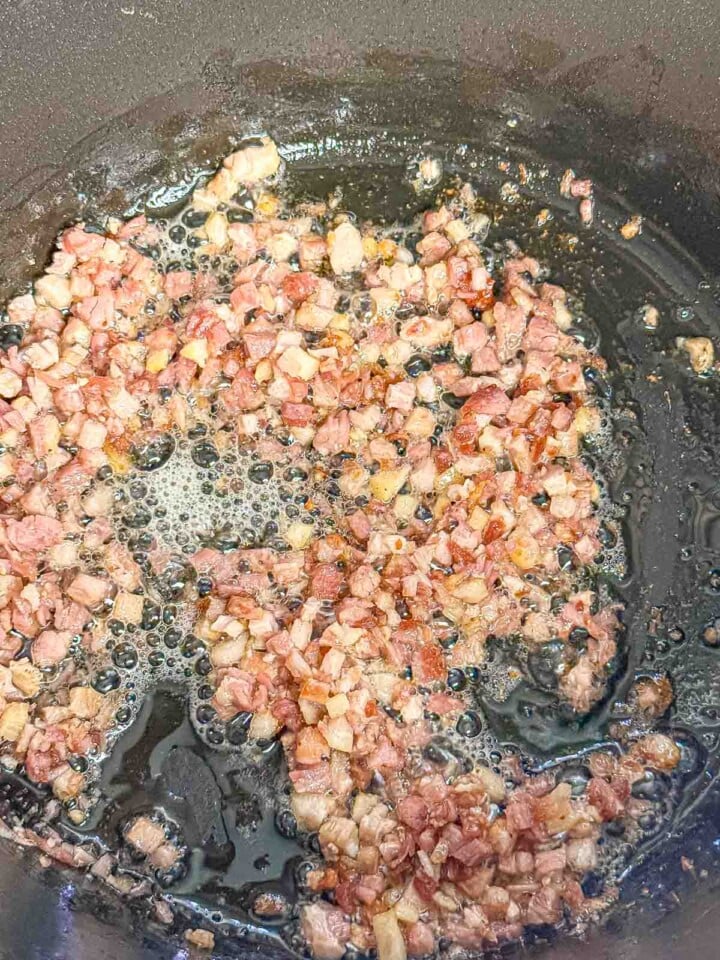 Diced pancetta cooks in a large pot until the fat renders and the edges begin to brown.