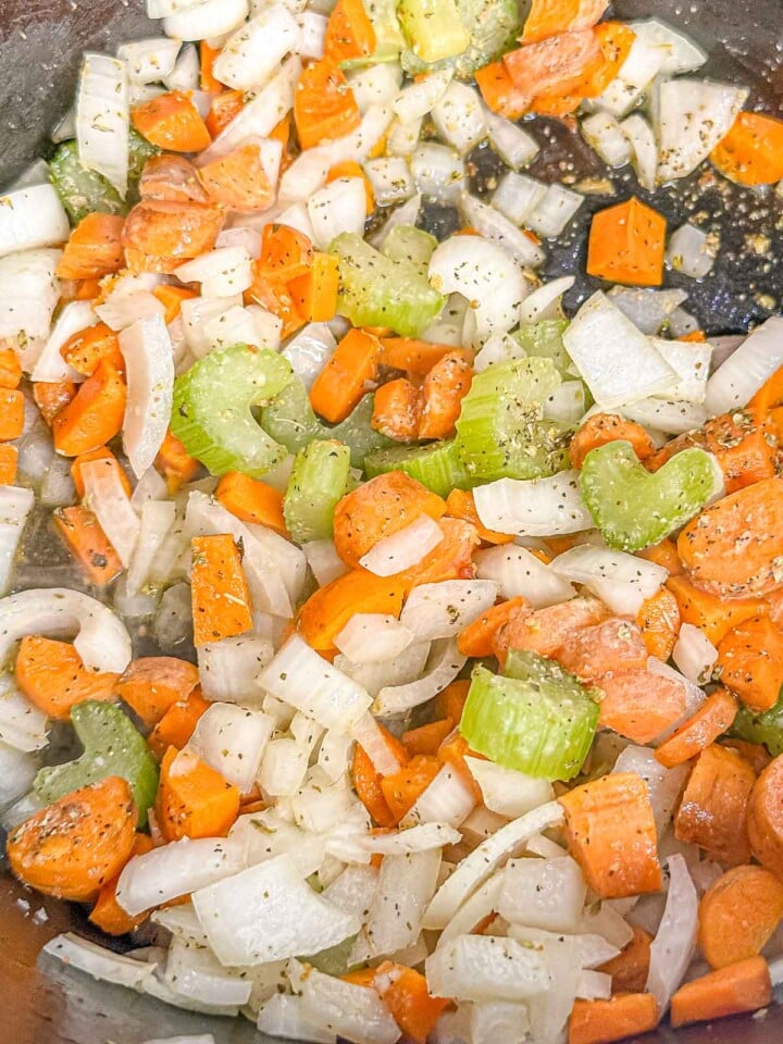 Chopped carrots, celery, and onion sauté with seasonings in a large pot.