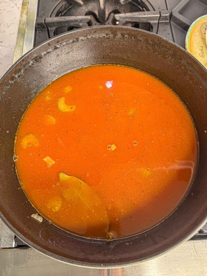 Chicken broth, passata, vegetables, and a bay leaf simmer together in a large pot.