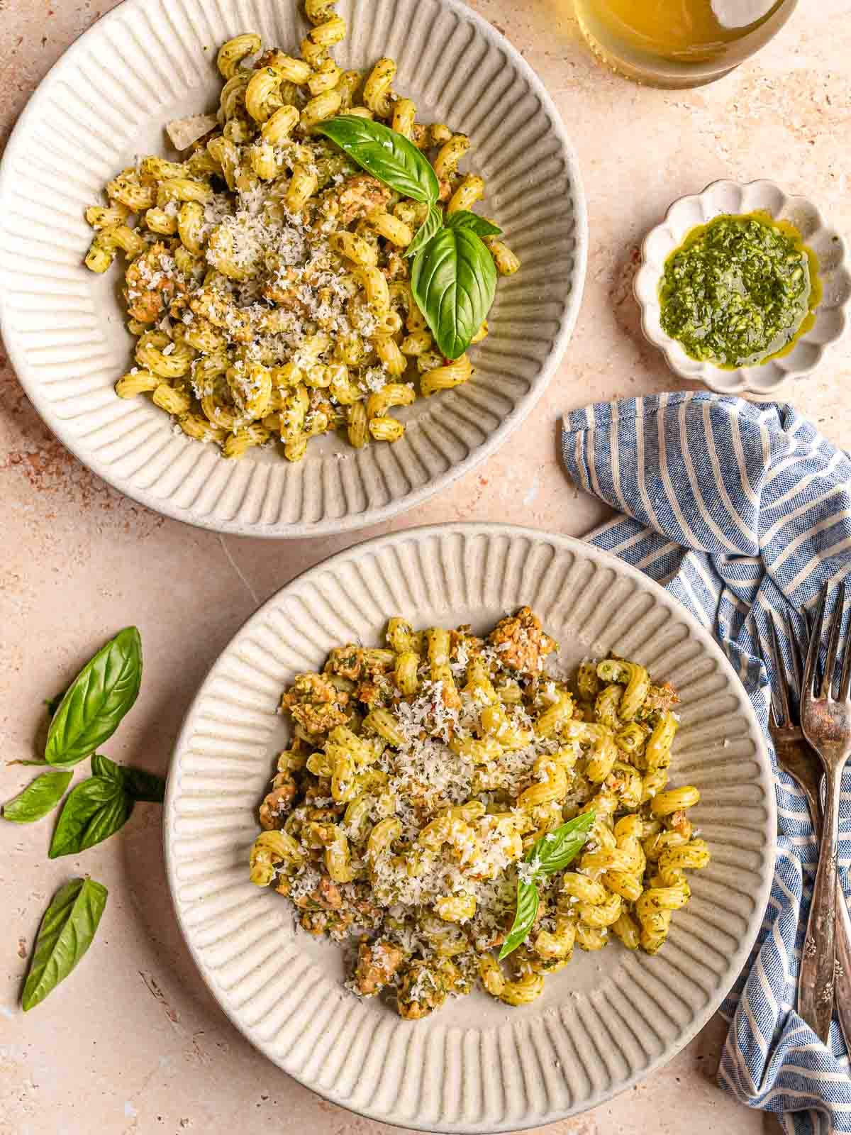 Two bowls of pesto sausage pasta served with Parmesan, basil and extra pesto.