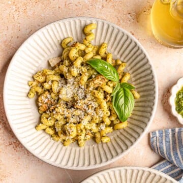 Bowl of pesto sausage pasta topped with grated Parmesan and fresh basil.