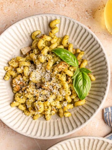 Bowl of pesto sausage pasta topped with grated Parmesan and fresh basil.