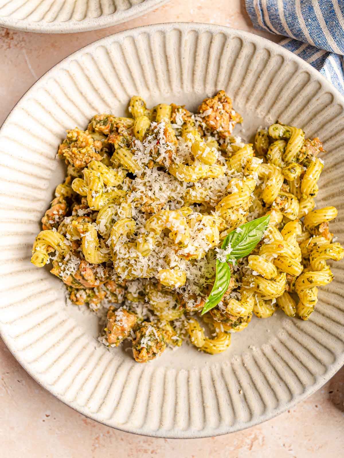Close-up of pesto pasta with Italian sausage, grated Parmesan and fresh basil.