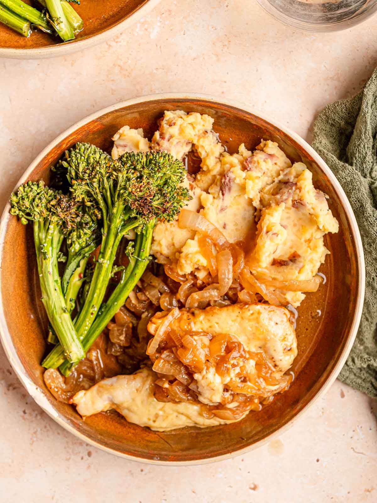 Close-up of French onion chicken topped with melted cheese and onions, served with mashed potatoes and broccolini.