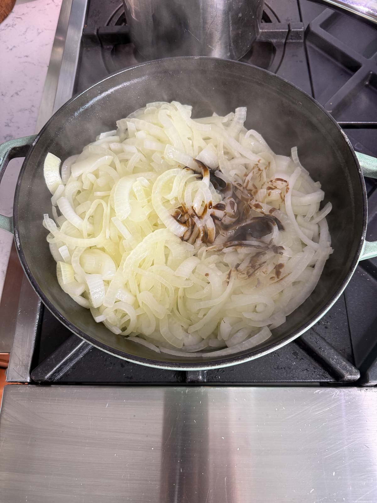 Sliced onions cooking in a skillet with seasonings and balsamic glaze.