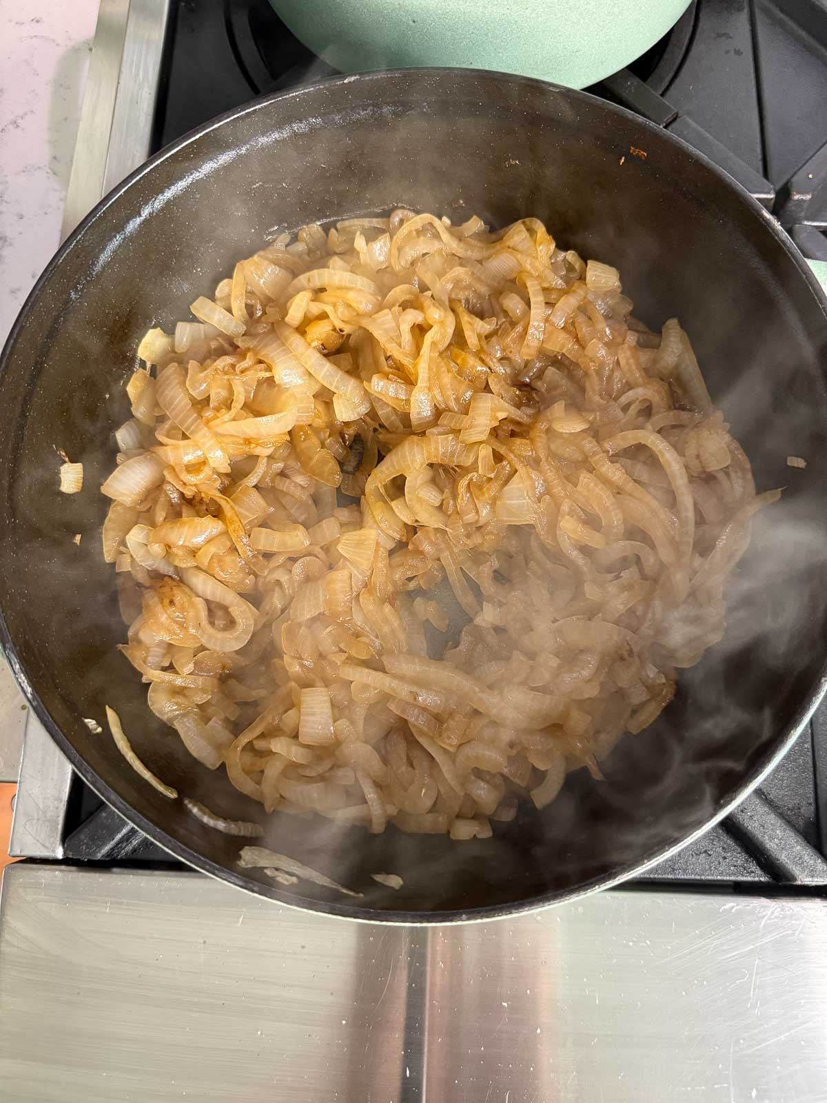 Golden caramelized onions cooking in a skillet on the stovetop.