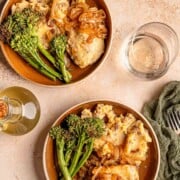Two plates of French onion chicken bake served with mashed potatoes and broccolini.