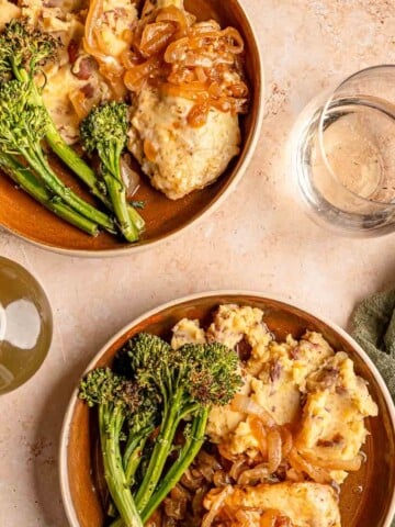 Two plates of French onion chicken bake served with mashed potatoes and broccolini.