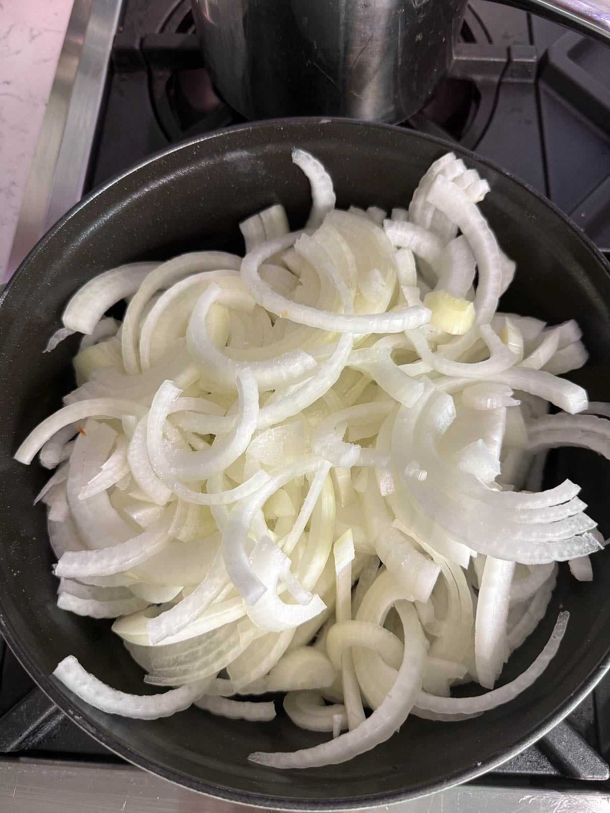 Sliced sweet onions piled in a skillet on the stovetop.