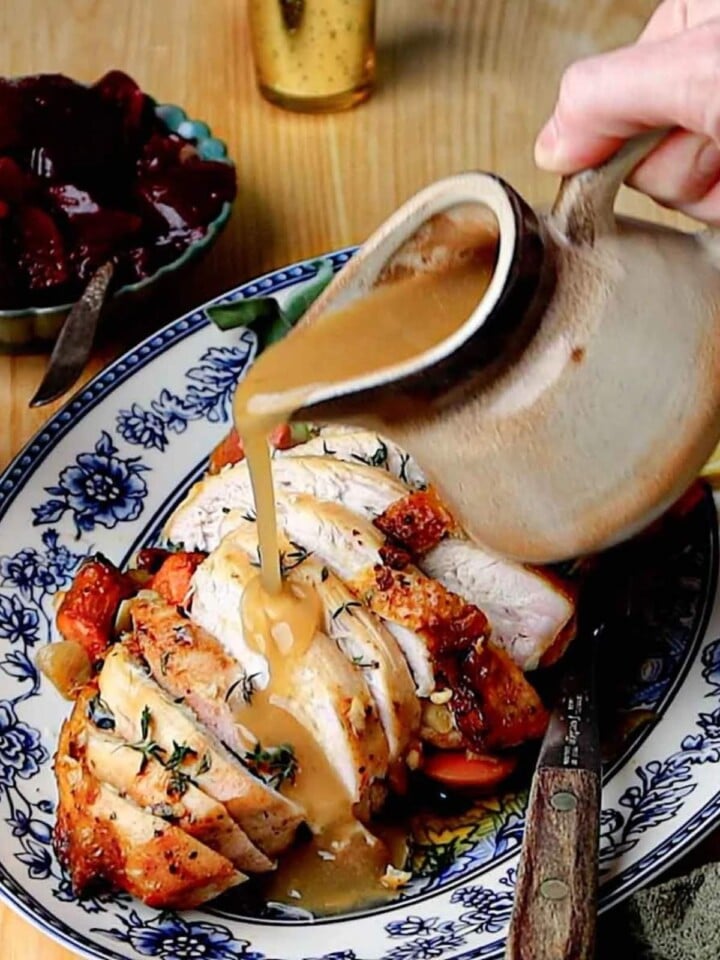 Gravy being poured over sliced roasted turkey breast with golden skin.