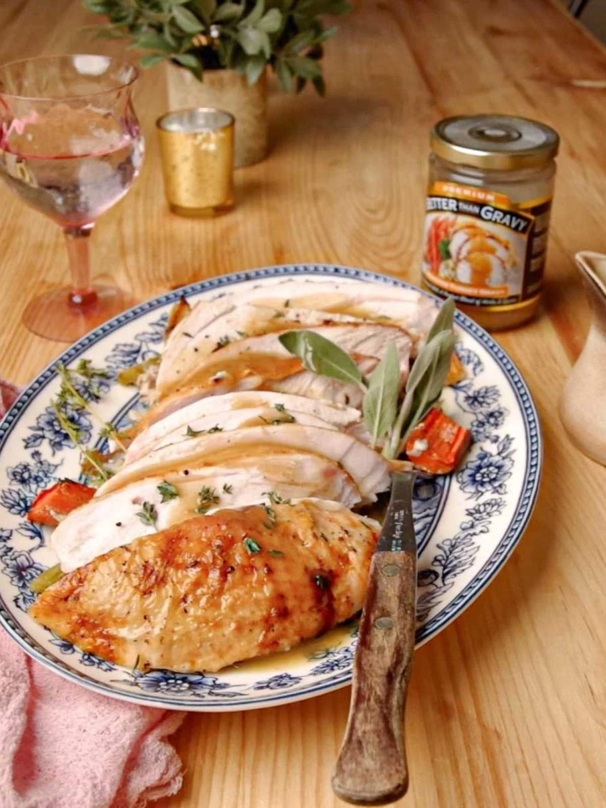 Sliced roasted turkey breast on a blue and white platter with fresh herbs and roasted vegetables.