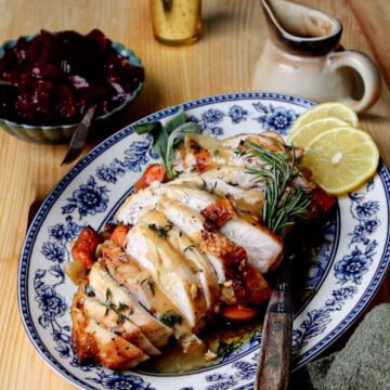 Sliced garlic herb roasted turkey breast with roasted vegetables, lemon slices, and rosemary.