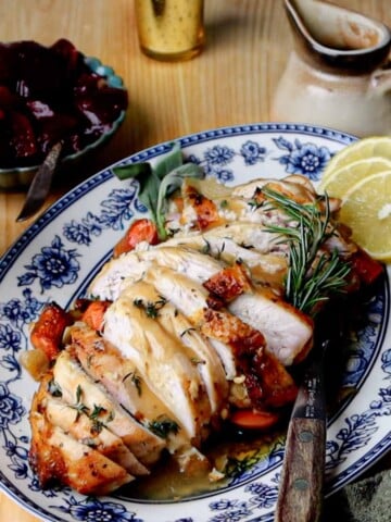 Sliced garlic herb roasted turkey breast with roasted vegetables, lemon slices, and rosemary.