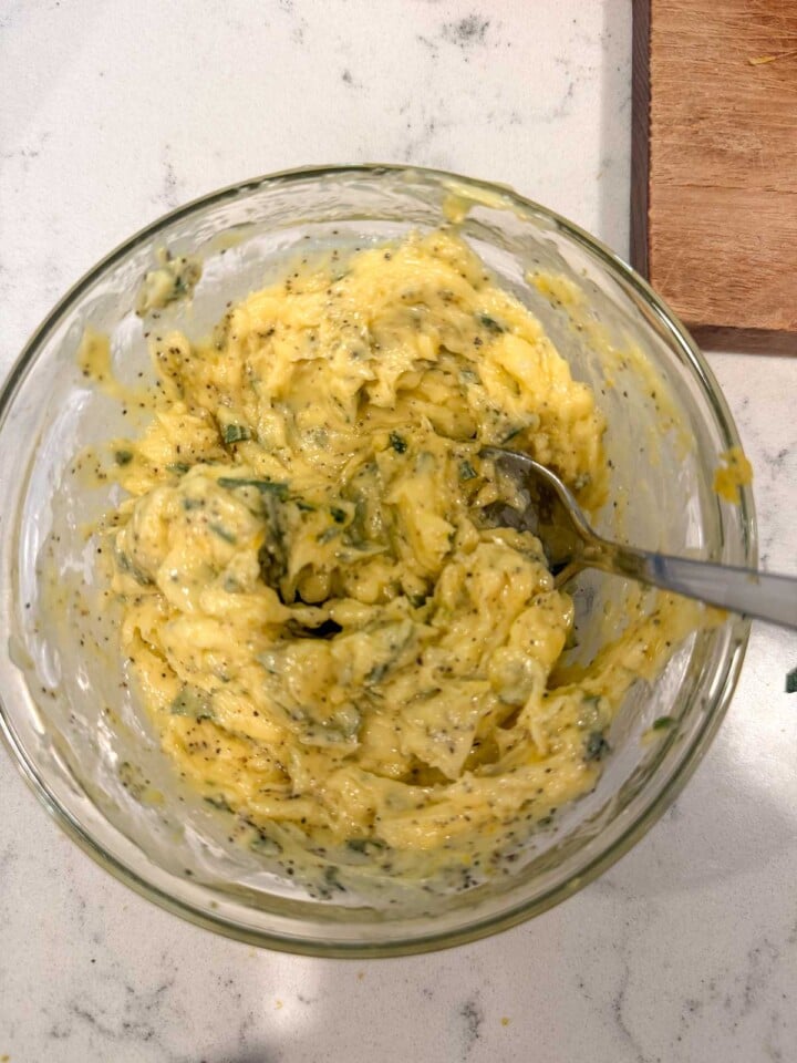 Garlic herb compound butter in a glass bowl with a spoon.