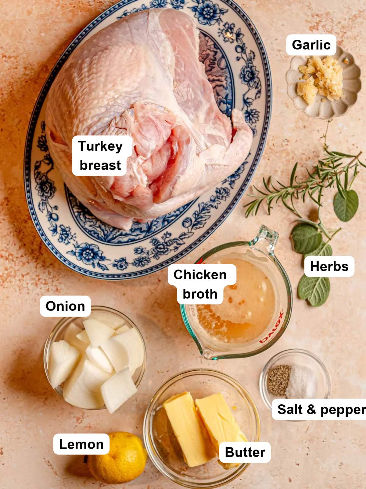 Turkey breast, butter, broth, onion, lemon, herbs, salt, and pepper arranged on a counter.